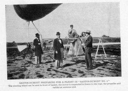 SANTOS-DUMONT PREPARING FOR A FLIGHT IN "SANTOS-DUMONT NO. 6" The steering-wheel can be seen in front of basket, the motor is suspended in frame to the rear, the propeller and rudder at extreme end.