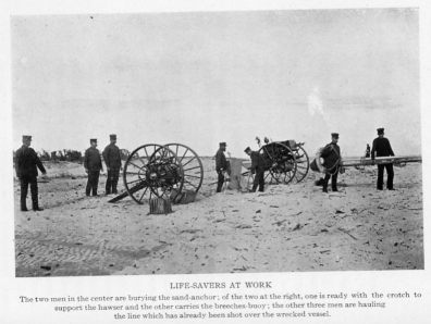 LIFE-SAVERS AT WORK The two men in the center are burying the sand-anchor; of the two at the right, one is ready with the crotch support the hawser and the other carries the breeches-buoy; the other three men are hauling the line which has already been shot over the wrecked vessel.