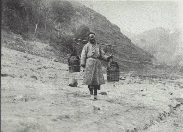 THE UBIQUITOUS WATER CARRIER  Drawing the water and hewing the wood are daily chores in China, mostly carried out by women—though this is a picture of a man, a half-wit