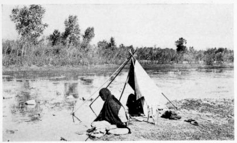 INDIAN WOMEN, POUNDING CLOTHES UPON THE ROCKS BESIDE A SHALLOW BROOK, CEASED THEIR WORK TO STARE