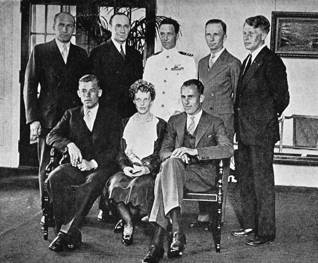 Photo wide indoor shot of 8 individuals;
                Stultz, Earhart, Gordon are seated; 5 are standing in
                back